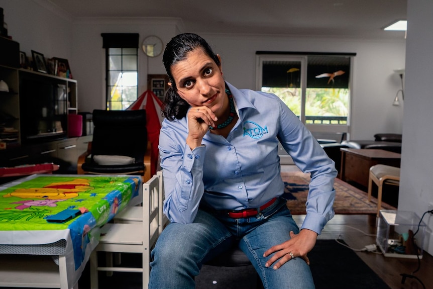 Andrea Gonzalez wearing casual business clothing, and leaning forward looking at the camera with a serious expression.