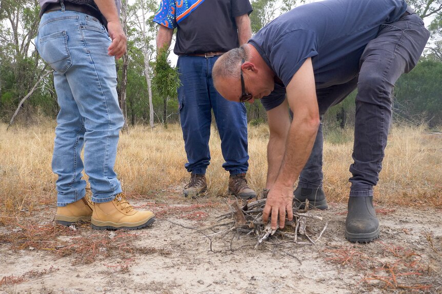 A man makes a small fire with two other nearby, Old Toomelah New South Wales, March 2024.