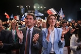 Man and woman clapping as crowd hold small French flags. 