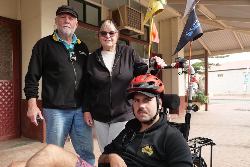 Two parents stand behind their son on a recumbent trike.