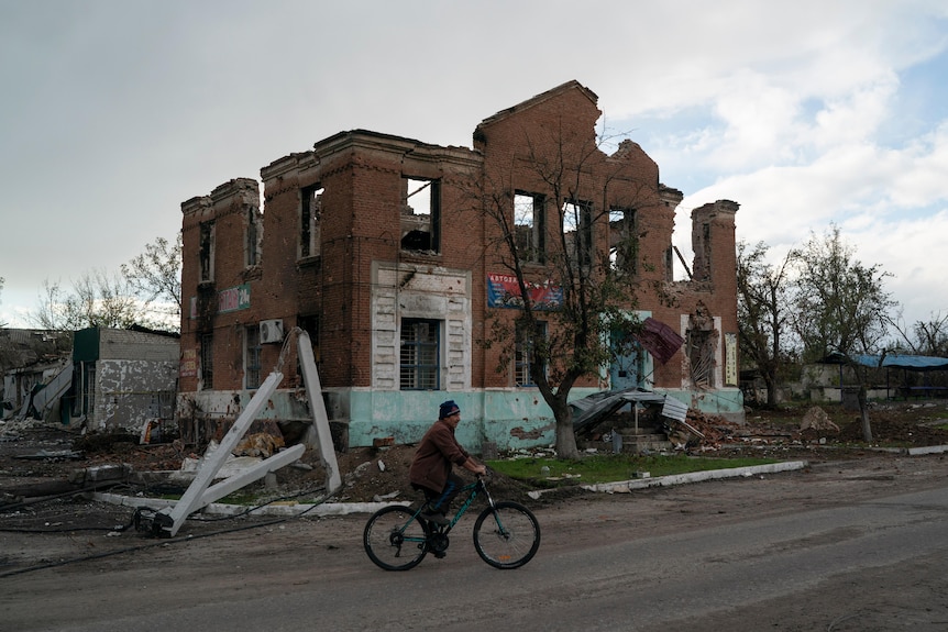 A man rides his bicycle past a damaged building in the village of Drobysheve.