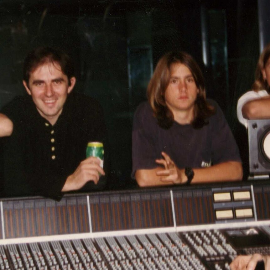 Young Silverchair members leaning over recording desk with producer and film maker