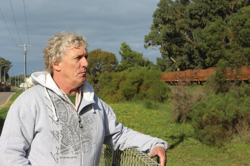 A man in a hoodie stands near a fence watching a train go past.