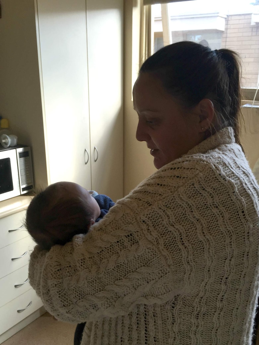 Kirsten holds her baby in her kitchen