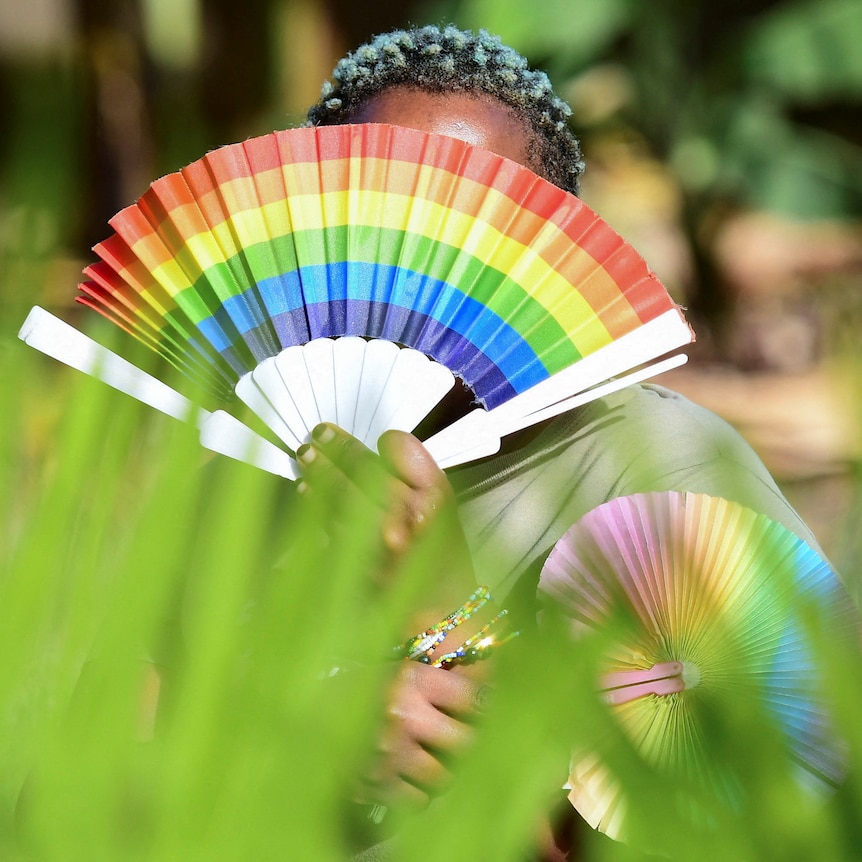 A woman hold a rainbow fan in front of her face.