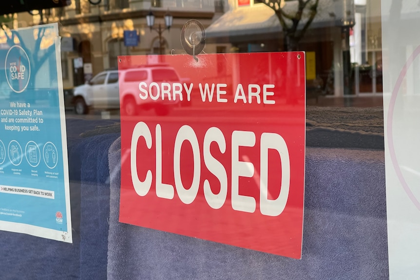 A red sign on a  glass window reads sorry we're closed