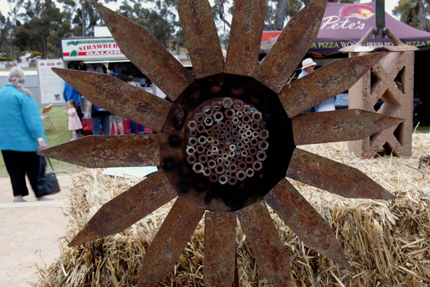 Metal artwork that resembles a sunflower sitting on a hay bale. 