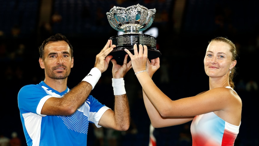 A male and female tennis player hold up a trophy.