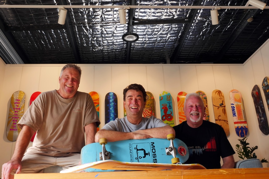 three men smiling with a skateboard