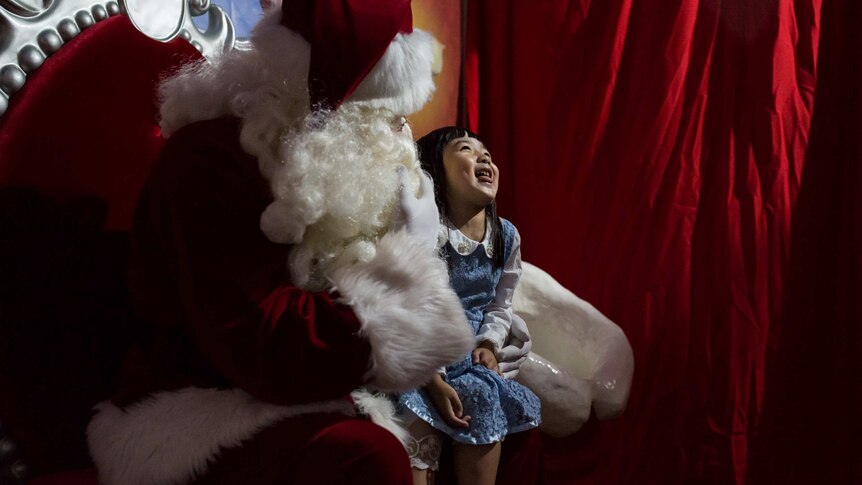A little girl squirms in delight on Santa's knee.
