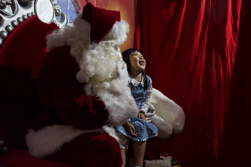 A little girl squirms in delight on Santa's knee.