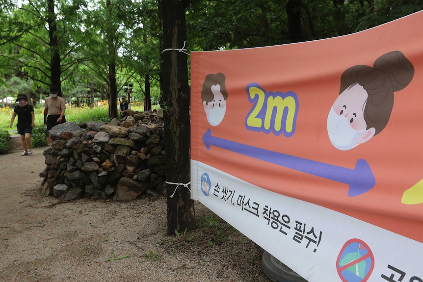 A cartoon banner with two faces with an arrow between them is strung up in a park.
