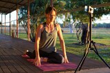 A woman performs a yoga pose on the verandah of a house on an outback property