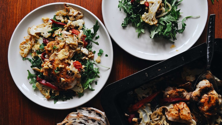 Two plates of rocket topped with baked chicken, capsicum and cauliflower, a healthy family tray bake recipe.