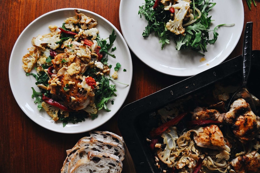 Two plates of rocket topped with baked chicken, capsicum and cauliflower, a healthy family tray bake recipe.