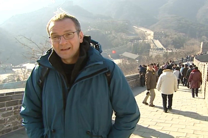 A reporter looking at the camera and on China's Great Wall.