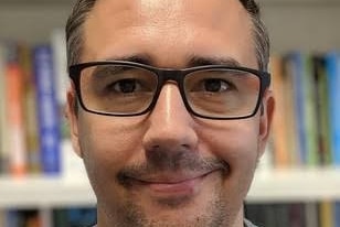 A man in glasses stands near a book shelf