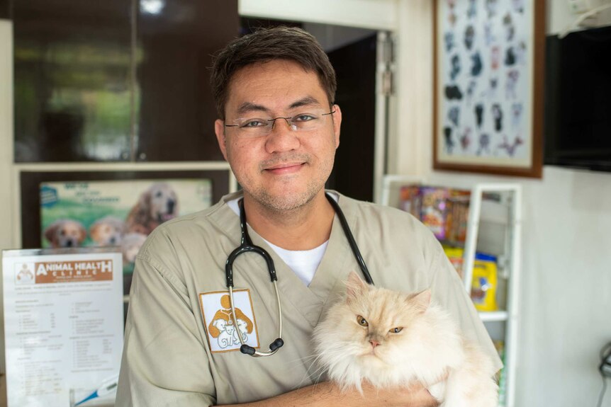 A smiling man in a vet uniform holding a mean-looking cat