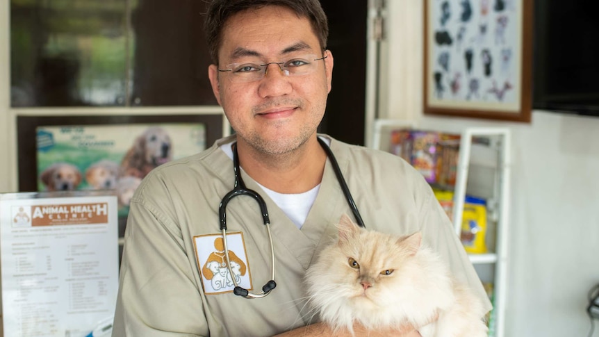 A smiling man in a vet uniform holding a mean-looking cat
