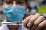 A man wearing a blue face mask holds up a vial of experimental COVID-19 vaccine.