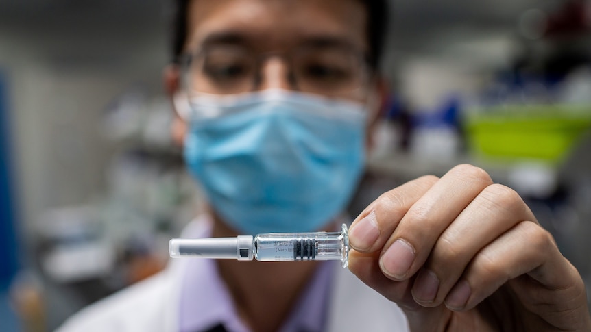 A man wearing a blue face mask holds up a vial of experimental COVID-19 vaccine.