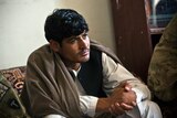 A man wearing Afghan clothing sits indoors listening intently.