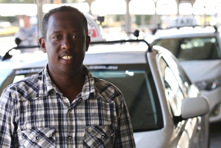 Taxi driver Mohamed wearing a checked long sleeve shirt, standing in front of his car.