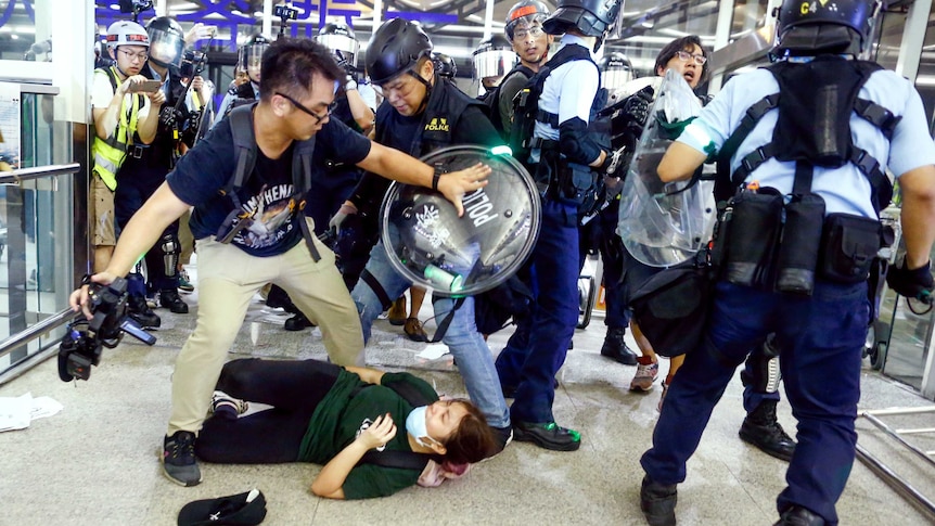 A man pushes back riot police at Hong Kong airport as a woman lays on the ground.