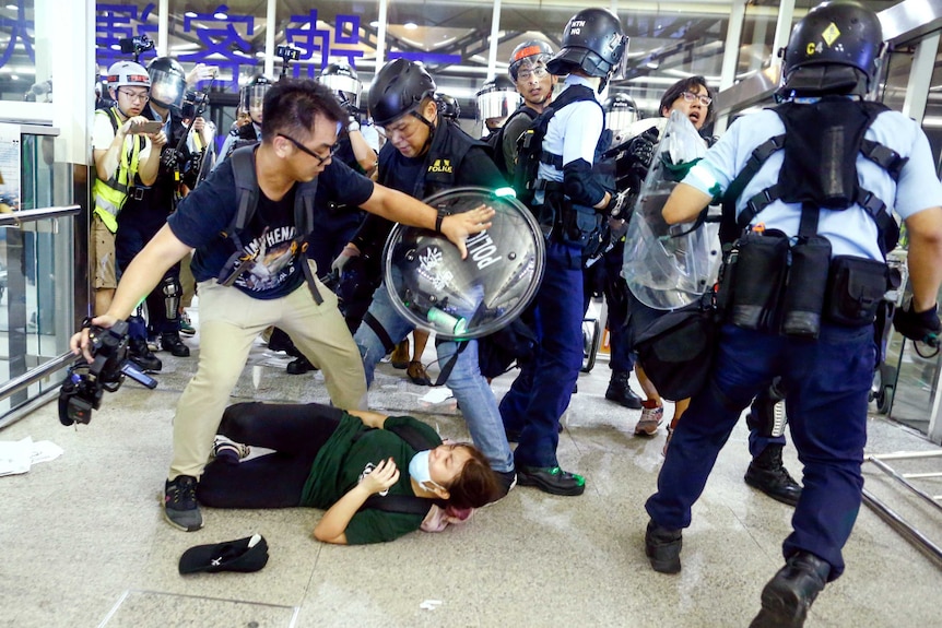 A man pushes back riot police at Hong Kong airport as a woman lays on the ground.