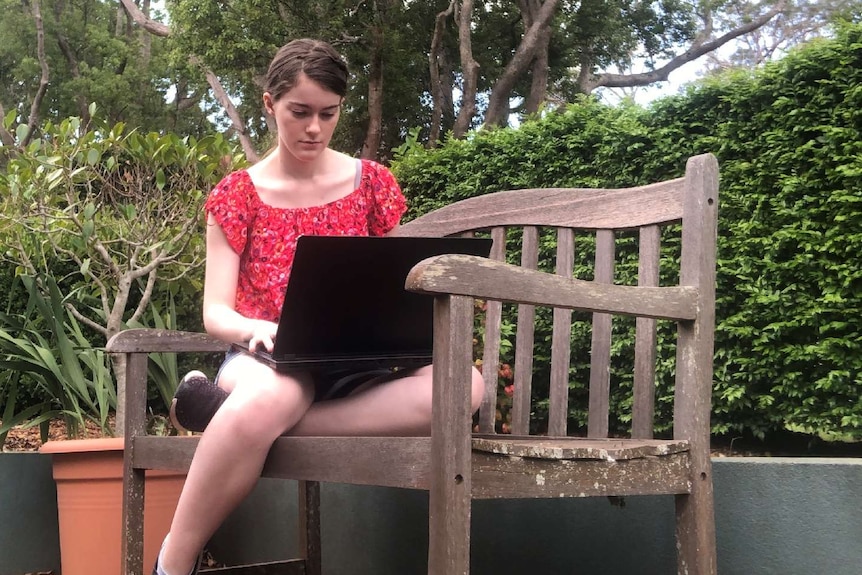 A young woman sitting on a park bench typing on a laptop