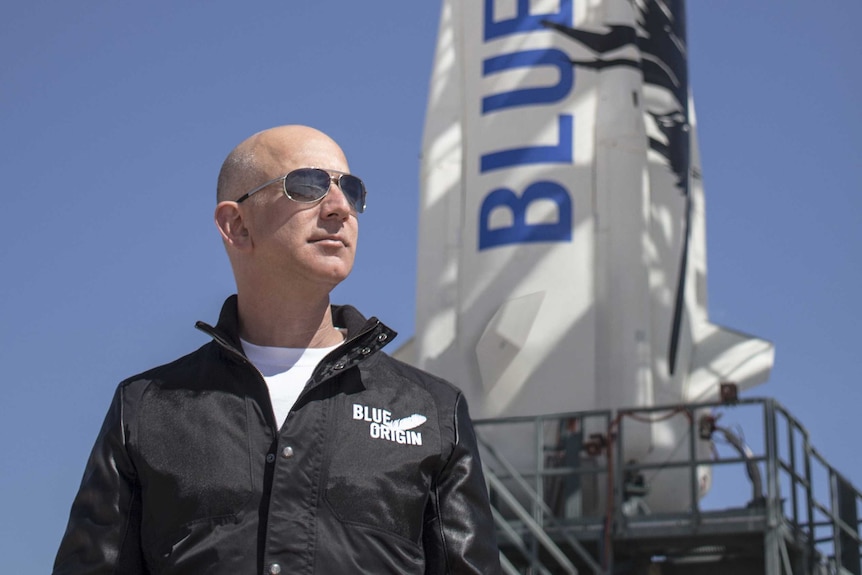 Billionaire Jeff Bezos wearing aviator sunglasses standing in front of a rocket