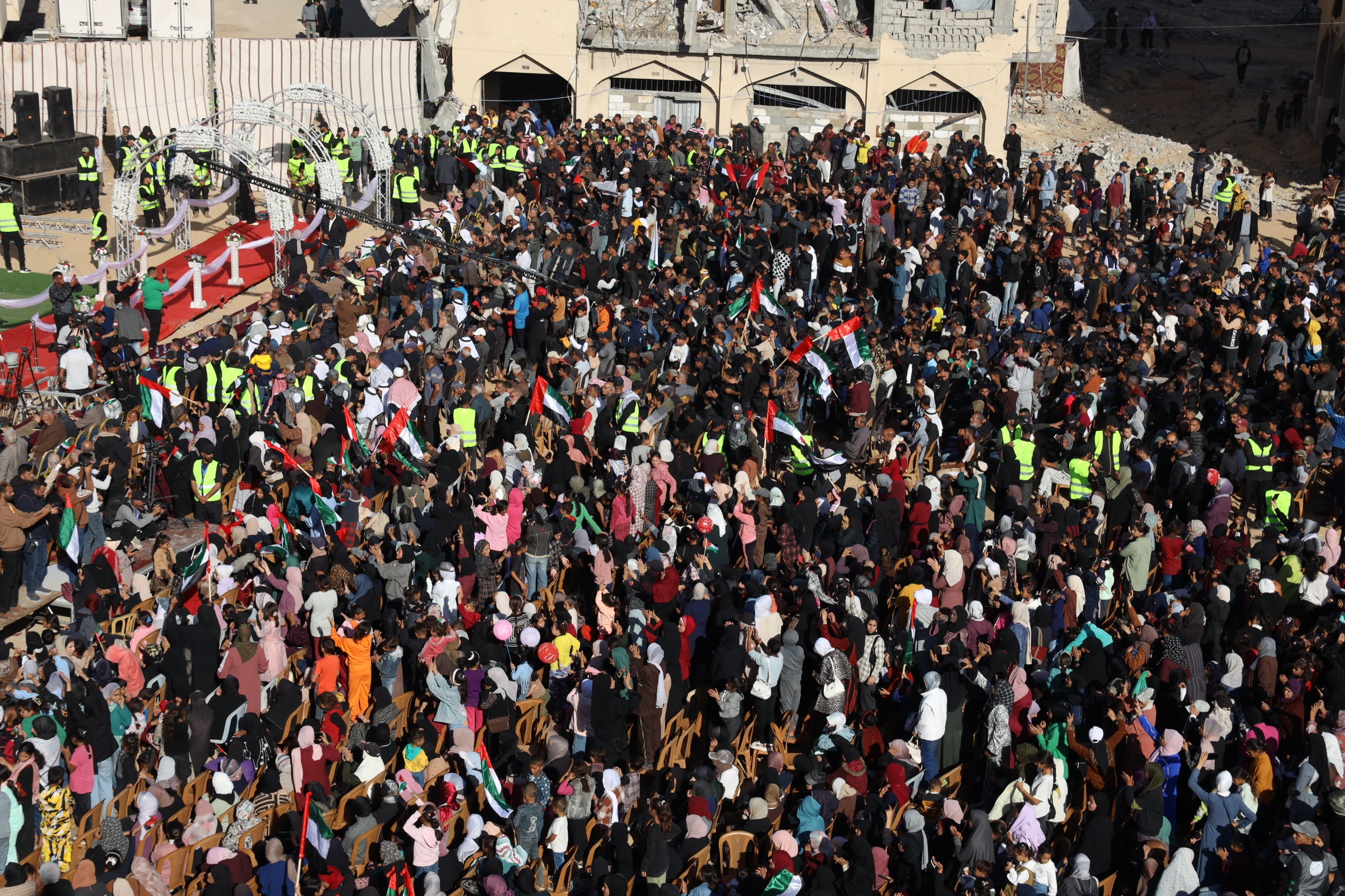 A top view of a giant crowd of people carrying flags in front of a red carpet aisle with a flower arch.