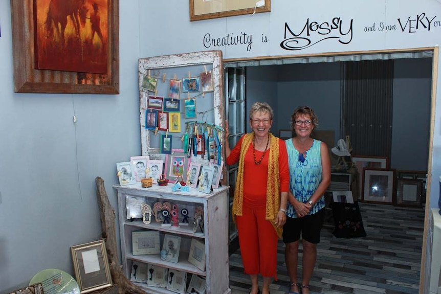 Two women smiling inside shop filled with colourful artworks and frames