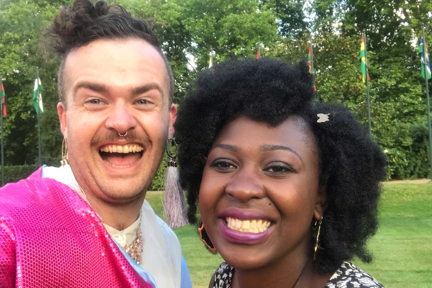 Two young people, one of whom is Thomas in their bright pink jacket, pose together for a selfie in garden grounds.