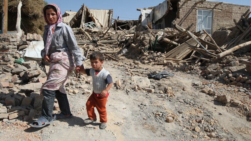 Iranian residents walk amongst the rubble of destroyed houses in a village after the quakes.