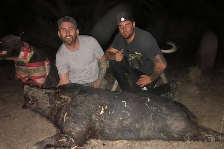 two men proudly show off a pig they have killed
