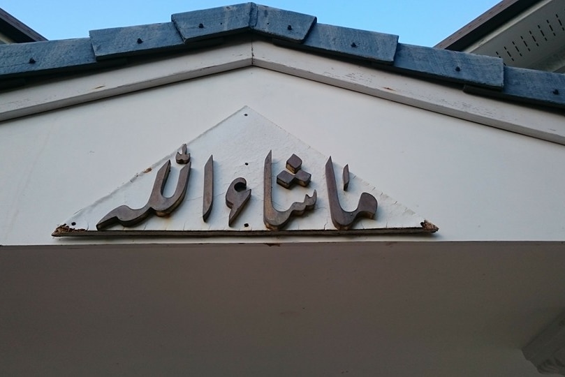 Wooden Arabic script under the eaves of a house, the script is a Pakistani greeting.