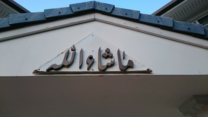 Wooden Arabic script under the eaves of a house, the script is a Pakistani greeting.
