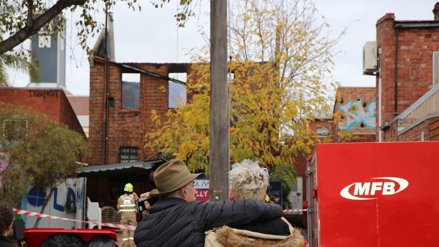 Two people with their backs to the camera embrace in front of La Mama Theatre, which was destroyed by fire.