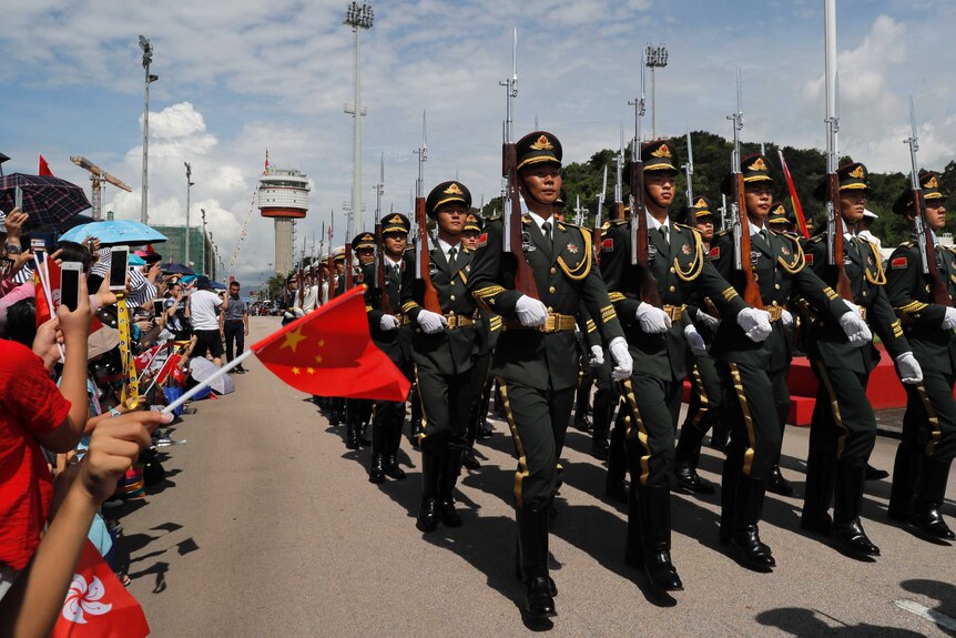 Chinese People's Liberation Army soldiers march in a line holding their guns up straight.