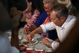 Roger Cook, in a white shirt, puts sprinkles on a cookie.