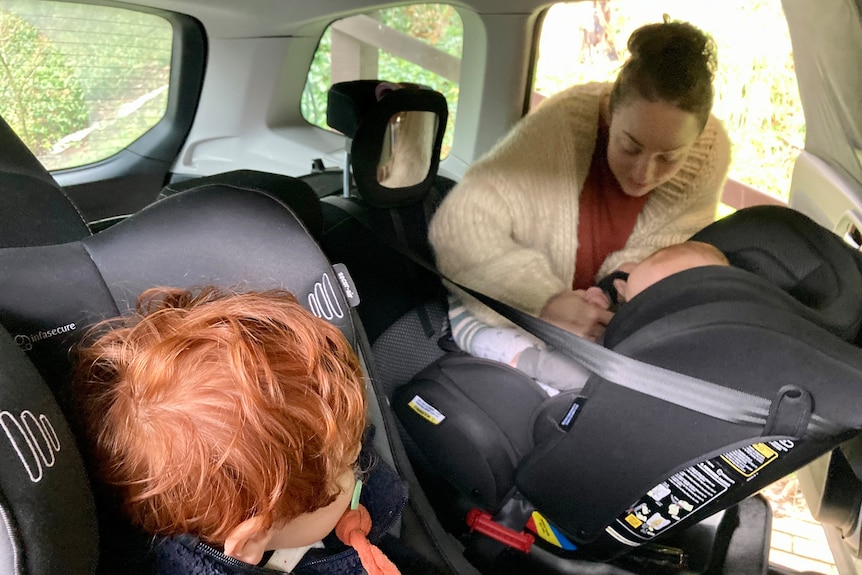 A mum clips her baby and three-year-old son into the car.