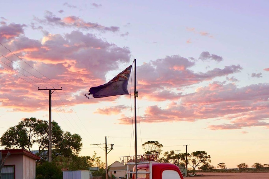 A red ute with an Australian flag on the back sits on red dirt near the Kingoonya Hotel.