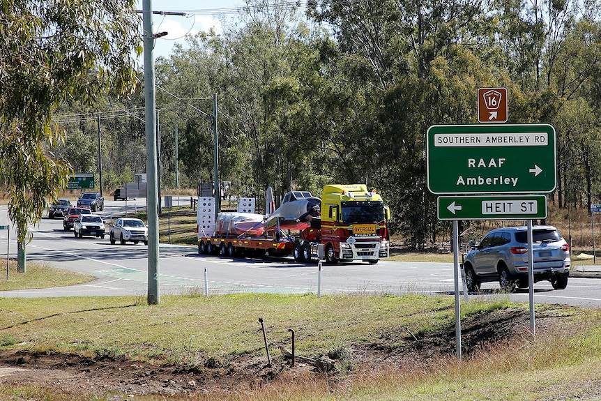 A plane, with its wings removed, on the back of a truck marked 'Oversize' driving down a road among traffic.