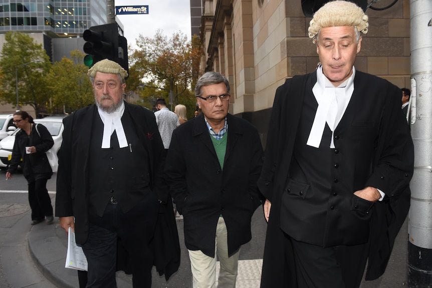 Aman Siddique, with his lawyers wearing wigs and robes either side, walking down a Melbourne street