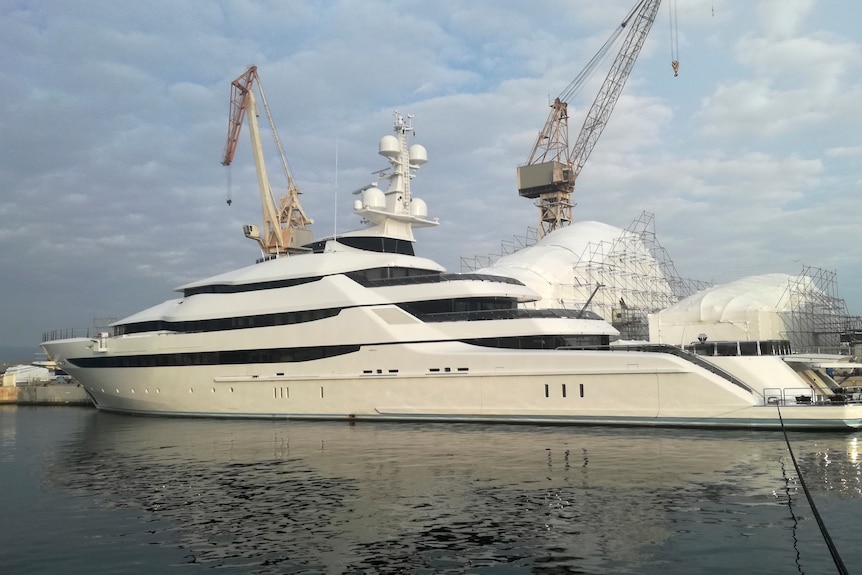 A white superyacht is seen docked near a crane