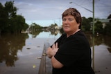 A woman stands in front of flood waters in Lismore.