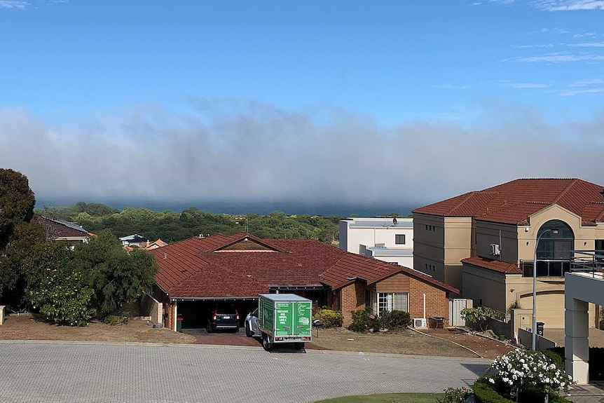 A cloud of fog can be seen off the coast with homes in the foreground.