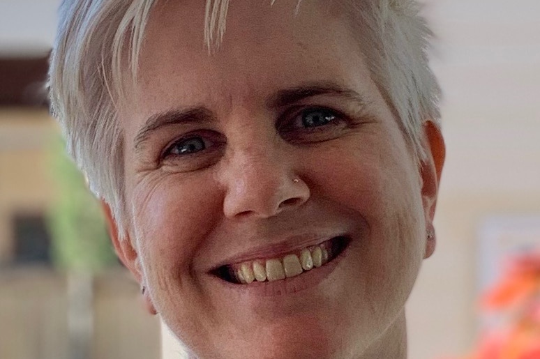 A woman with short blonde hair smiles at the camera.