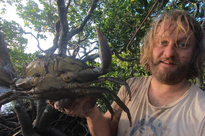 A man holding a large crab by the back legs.